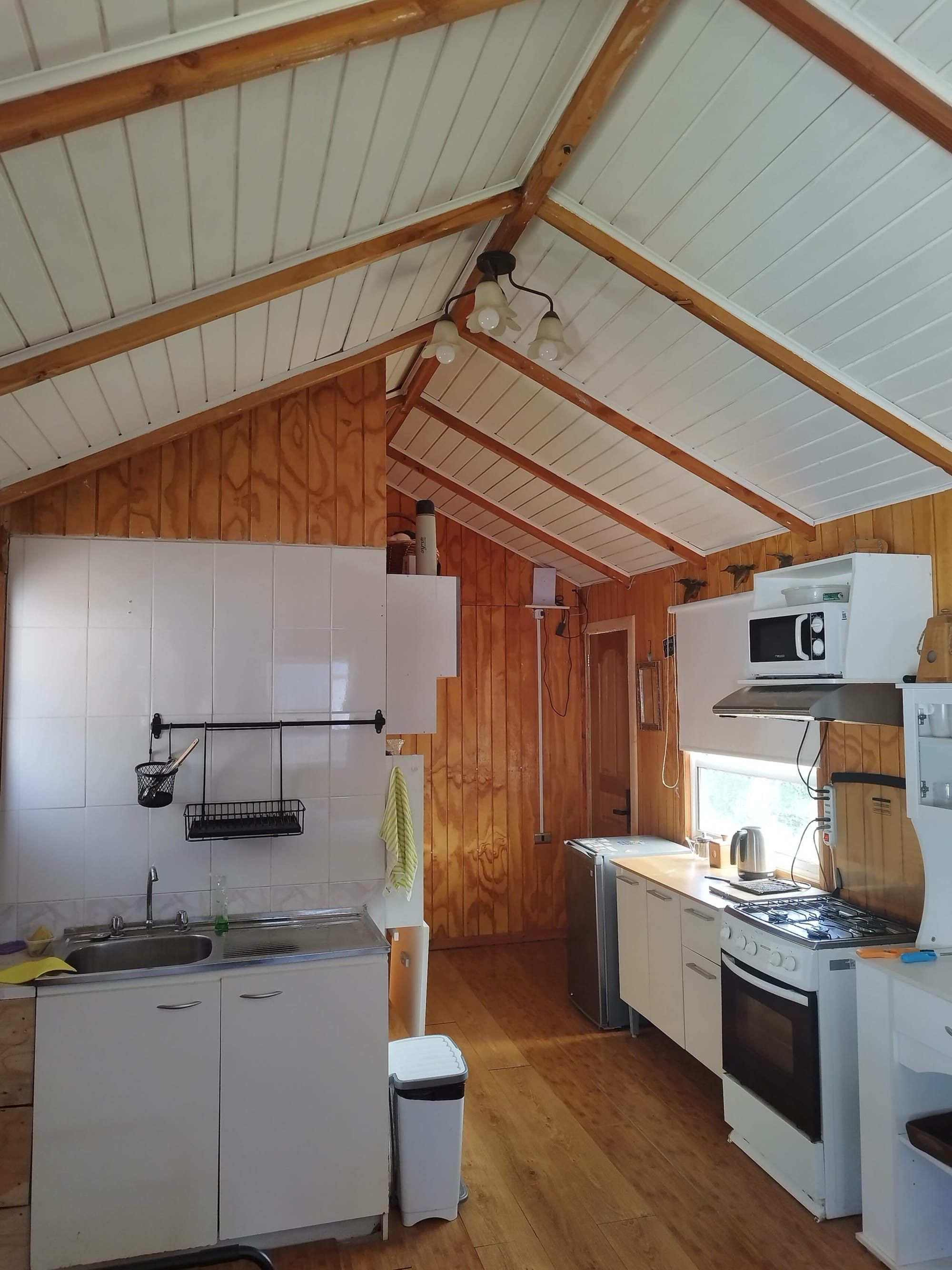 La cocina con azulejos blancos, microondas y cocina a gas bajo el cielo de madera