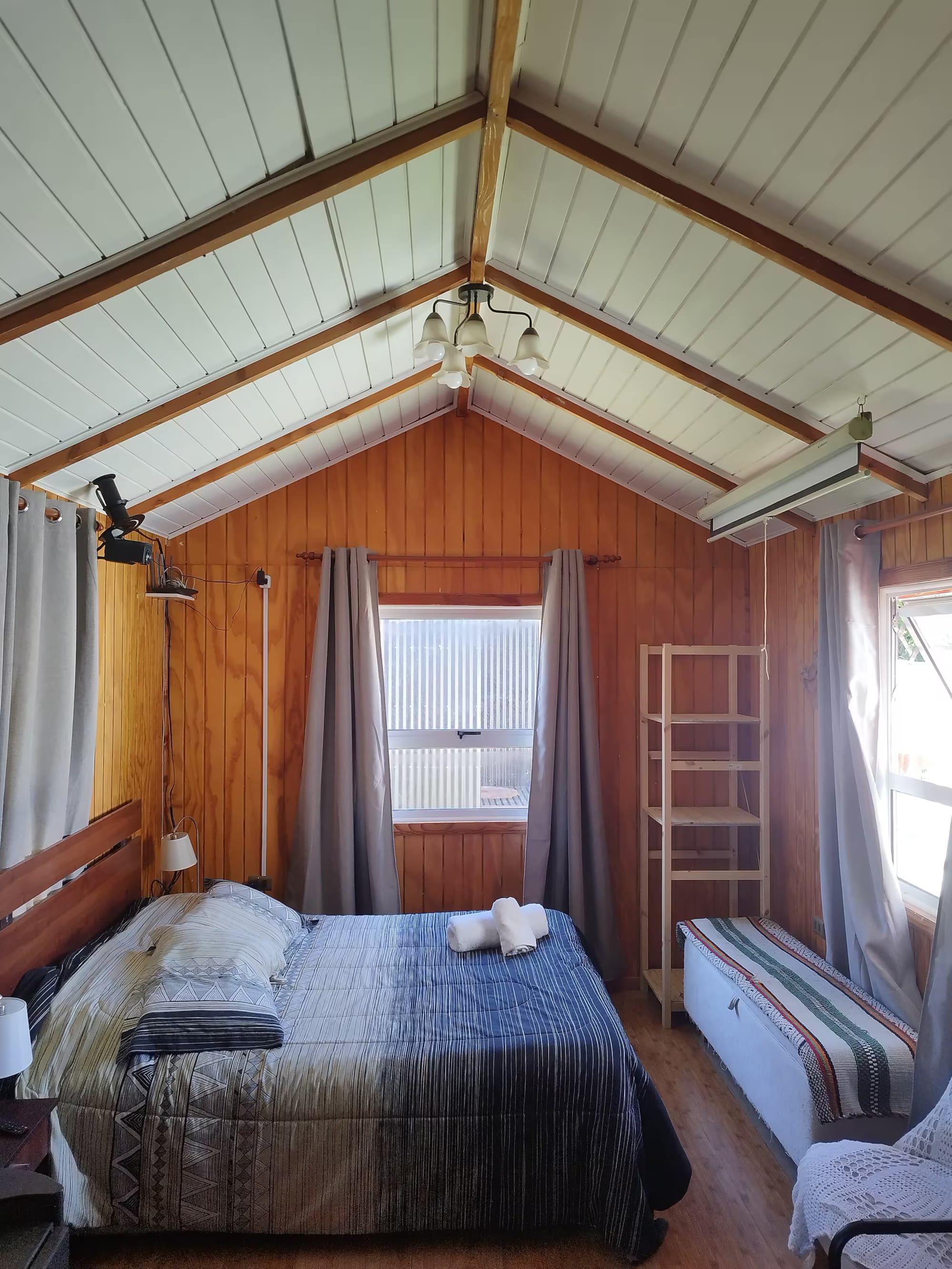 El interior con la cama, el cielo a dos aguas de madera y las ventanas con cortinas